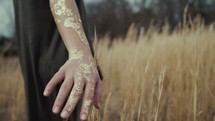 a woman with gold glitter on her hands running her hands through brown grasses 