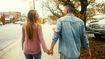 a couple walking down a sidewalk holding hands 