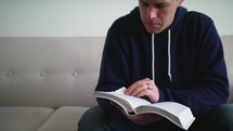 a man sitting on a couch reading a Bible 