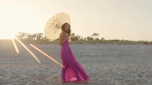 Fashion Girl On Summer Beach At Sunset with pink dress and yellow umbrella