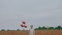 a woman walking through a field carrying red balloons 