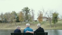 elderly men sitting on a park bench talking 
