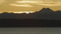 Sunset behind Olympic mountain range with forest and water in front