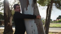 Man Dressed in Black Hugs a Tree in the Countryside