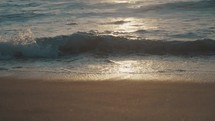 Ocean waves gently rolling on to a sandy beach shore at a sunset.