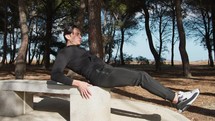 Man Does Abs Exercises On A Marble Bench In The Park