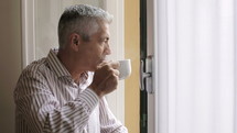 man looking out a window and drinking coffee