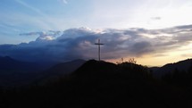 Aerial view of a Christian cross on a rock in a mountain rural landscape at sunset