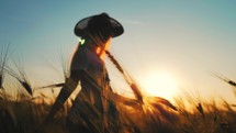 Concept of children's happiness. Silhouette young girl in the wheat field. Happy child play in the field at sunset. Happy kid playing in the wheat field on a warm summer day at sunset.