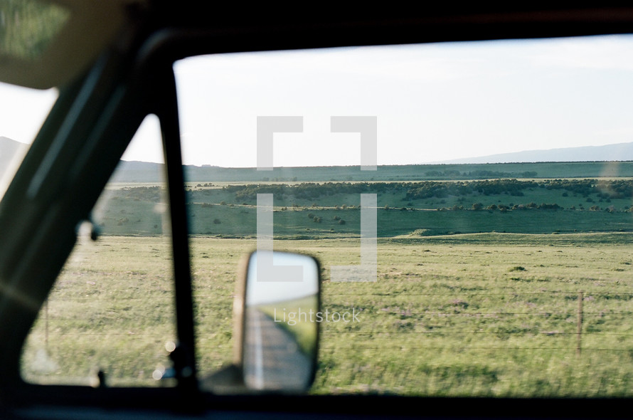 view of hills and prairies through a car window 