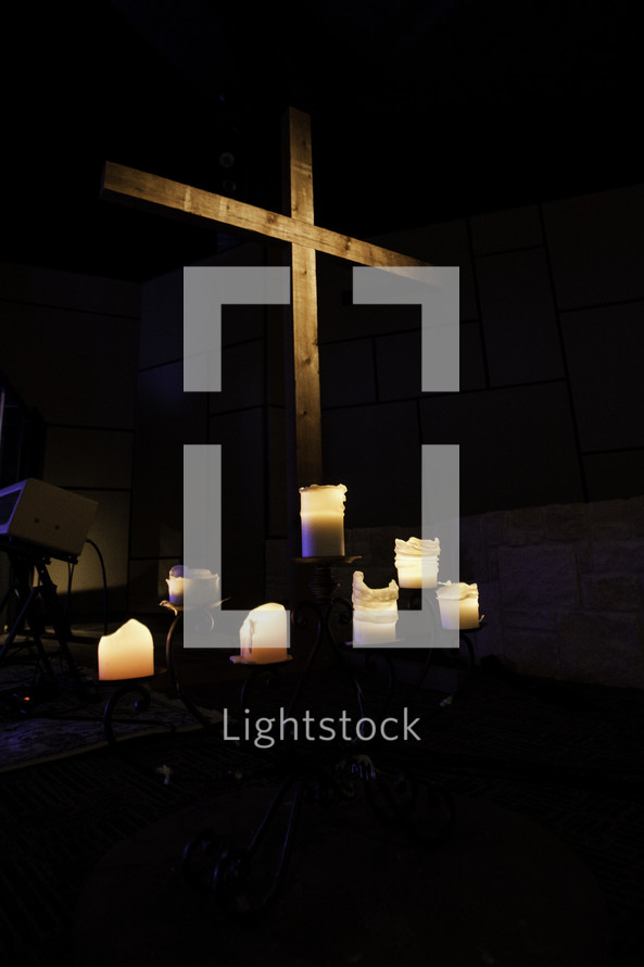 Wooden cross with six lit, white candles at the base.