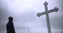 Young man in black suit looking at cross praying in worship in cinematic slow motion.