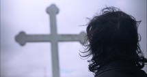 Young man in black suit looking at cross praying in worship in cinematic slow motion.