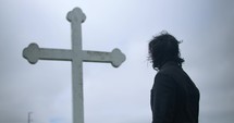 Young man in black suit looking at cross praying in worship in cinematic slow motion.