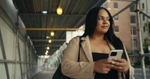 Young business woman walking around the city using her phone and laptop