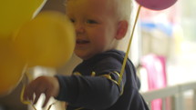 A baby girl in a crib playing with balloons