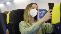 Woman in respiratory mask travelling on an airplane during pandemic times takes a selfie.