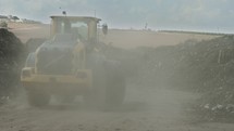 Industrial compost production site. Tractors loading compost into screening machines and trucks. Slow motion