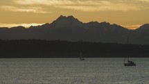 Two sailboats in front of Olympic mountains as sunset light fades