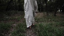 Jesus Christ dressed in white robe, or biblical prophet like Moses, Elijah, Abraham, walking in dramatic slow motion in wooded area surrounded by trees and green grass.