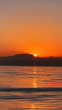 Sunrise Timelapse in the sea. Sun is raising behind the mountains.