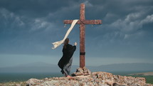 A woman in a black cape approaches the Holy Cross on a stormy day. Pan shot
