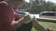 a man sitting in a park reading a Bible 
