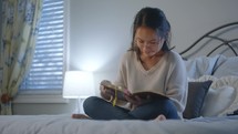 a young woman sitting on her bed reading a Bible 