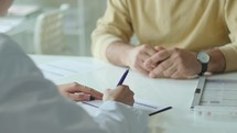 Hands of Female Doctor Interviewing Patient and Writing Medical Records
