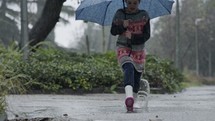 Slow motion of a little girl skipping in puddles holding an umbrella in the rain