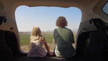 Brother and sister sitting in the back of a car over looking a farm