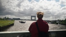 Woman Standing On The Bridge Looking At The IJ River And Port In Amsterdam, Netherlands, Europe. - medium shot