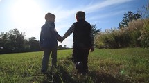 boys walking holding hands in a field outdoors 