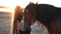Young blonde girl with long hair stroking and hugging horse. Slow motion. Beautiful young woman with dark stallion on nature. Love and friendship concept
