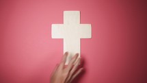 placing simple wooden cross on a pink background 