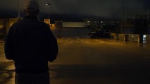 A lonely depressed man walking through a parking lot on a damp night