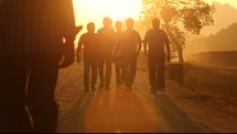 men walking down a dirt road at sunset 