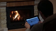 a man sitting in front of a fireplace using a tablet 