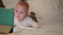 Cute baby girl lying on a bed and watching on tablet screen