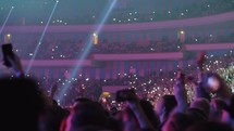 Crowded concert hall, music fans waving lights to music