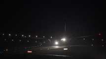 Commercial airplane moving down a taxiway at night.