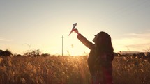 Girl plays with paper plane at Sunset