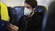 Traveller in the airplane in mask putting on earphones to listen to the music.