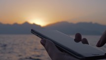 Woman using cellphone on sea and sunset background