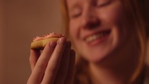 A smiling young woman enjoying a heart shaped Valentine's Day cookie 