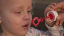 A closeup of a girls face blowing soap bubbles