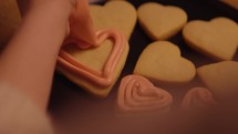 Young woman decorates heart shaped cookies with icing and sprinkles for valentines day