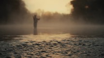 Young fly fisherman casting on a foggy river at sunrise