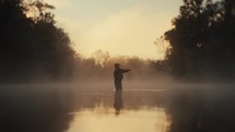 Young fly fisherman casting on a foggy river at sunrise