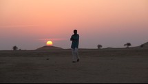 a man walking in the desert at sunset 